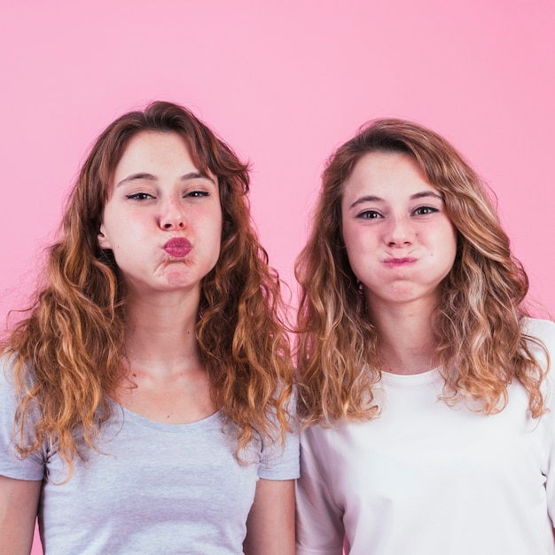 Gratis foto twee vrouwelijke vrienden die wang blazen tegen roze achtergrond