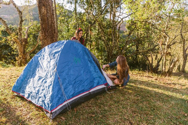 Twee vrouwelijke vrienden plaatsende tent terwijl het kamperen in bos