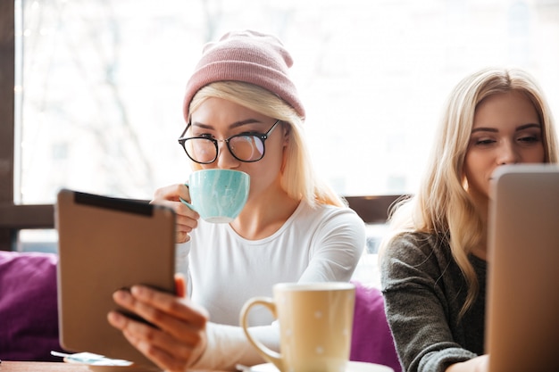 Twee vrouwen die koffie drinken en tablet in koffie gebruiken