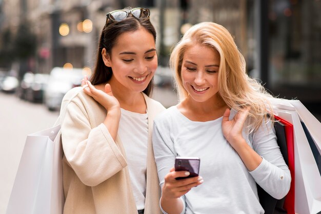 Twee vrouwen houden boodschappentassen en kijken naar smartphone