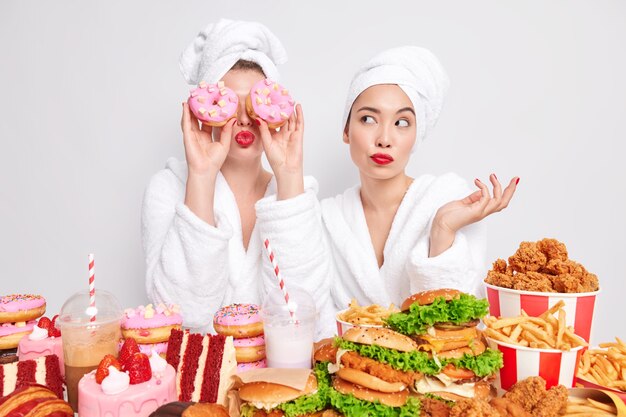 Twee vrouwen poseren in de buurt van een tafel vol heerlijke smakelijke snacks, geven de voorkeur aan een cheat-maaltijd in plaats van een gezonde.