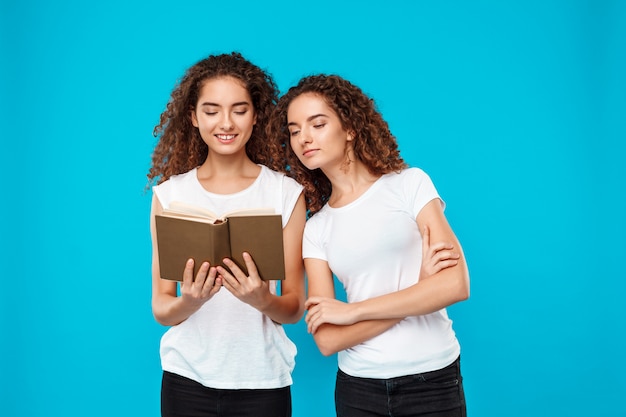 Twee vrouwentweelingen glimlachen, die boek over blauw lezen.