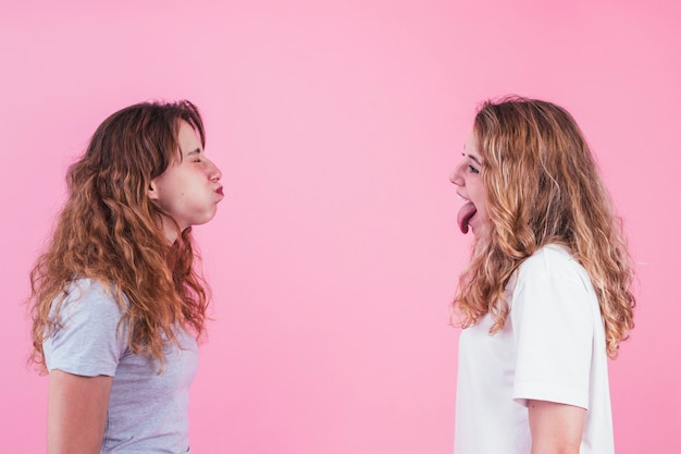 Twee zus plagen elkaar tegen roze achtergrond