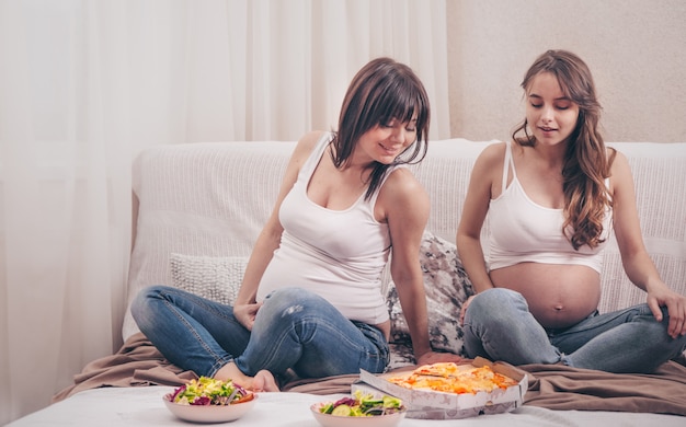 Twee zwangere vrouwen thuis eten van pizza en salade