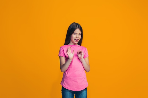 Twijfelachtig peinzend meisje dat iets verwerpt tegen oranje muur