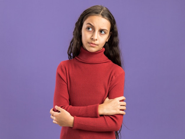 Twijfelachtig tienermeisje staande met gesloten houding kijkend naar kant geïsoleerd op paarse muur met kopieerruimte