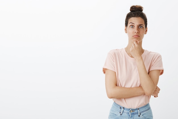 Twijfelachtige en clueless jonge stijlvolle vrouw poseren tegen de witte muur