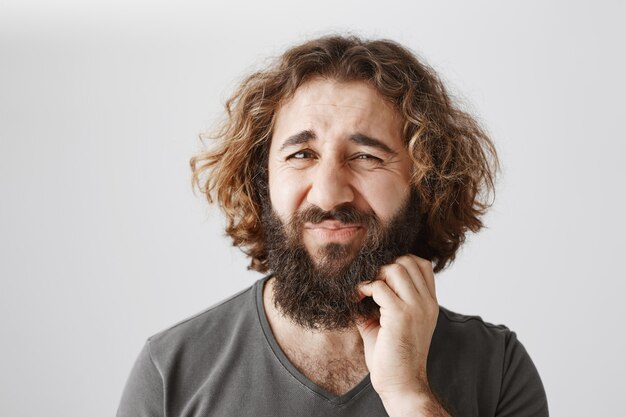 Twijfelachtige man uit het Midden-Oosten krabt aan zijn baard en fronst perplex