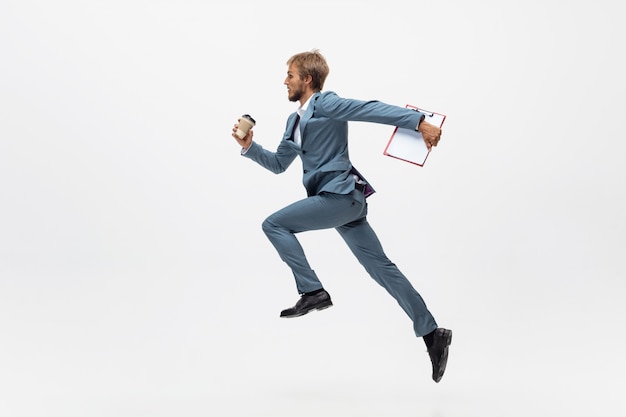 Typen. Man in kantoor kleding lopen, joggen op witte ruimte zoals professionele atleet, sportman. Ongewone look voor zakenman in beweging, actie met bal. Sport, gezonde levensstijl, creativiteit.