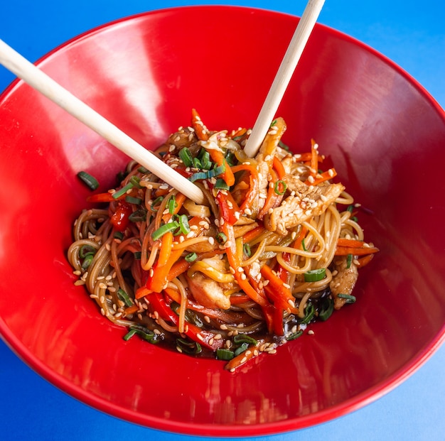 Udon roergebakken noedels met kip paprika wortel lente ui sojasaus en sesam in een kom