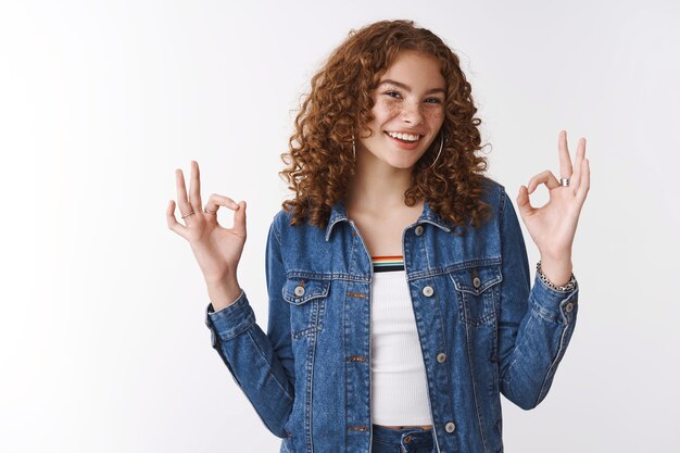 Uitgaand vriendelijk blij lachend roodharig meisje met sproeten puistjes dragen spijkerjasje lachen plezier hebben gevoel geweldig laten zien oke ok cool gebaar blij goed perfect resultaat, witte achtergrond