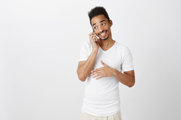 Uitgaande knappe zwarte man in wit t-shirt praten over de telefoon, glimlachen, gelukkig gesprek