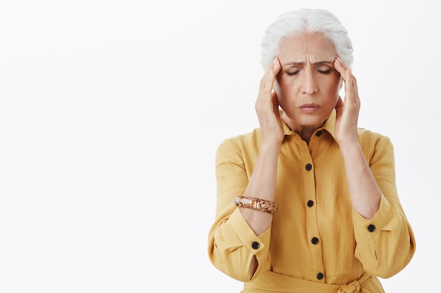 Uitgeput senior vrouw raakt haar hoofd aan, klaagt over migraine, heeft hoofdpijn