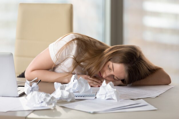 Uitgeput vermoeide vrouwenslaap bij bureau na overwerk in bureau