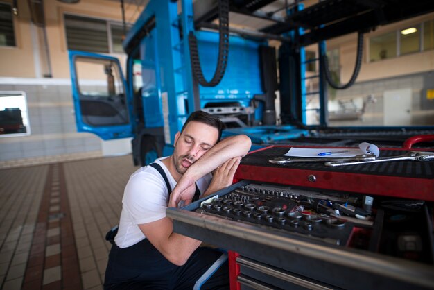 Uitgeputte automonteur die in slaap valt in zijn werkplaats