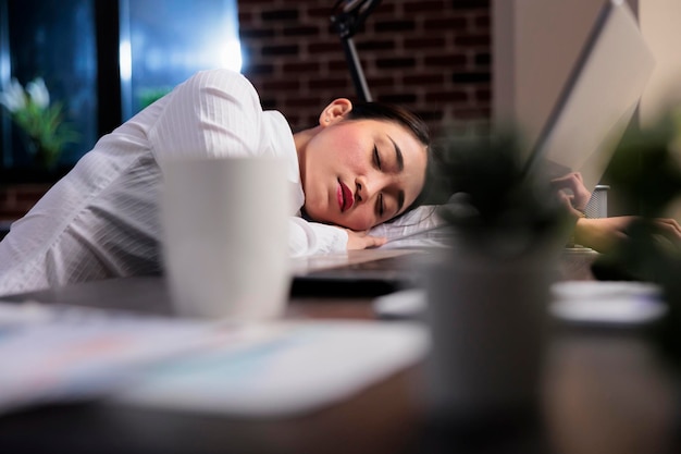 Uitgeputte uitvoerend manager met burn-outsyndroom die op het werk rust vanwege overwerk. Moe vermoeide zakenvrouw slapen op bureau in kantoorwerkruimte na overwerk