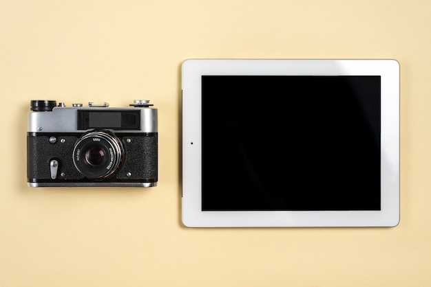 Gratis foto uitstekende camera dichtbij de digitale tablet met lege zwarte het schermvertoning op beige achtergrond