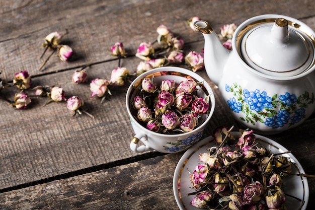 Uitstekende theepot en kop met bloeiende theebloemen op houten achtergrond