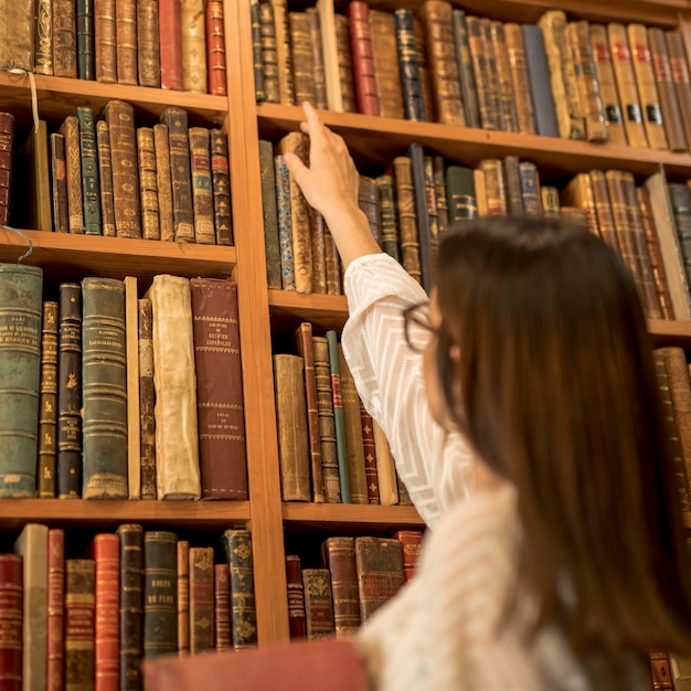 Gratis foto uitstekende vrouwelijke student die uitstekend boek in bibliotheek kiest