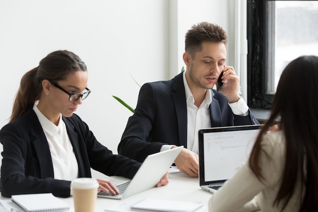 Uitvoerende bedrijfsmensen die laptops voor het werk met behulp van, die op telefoon spreken