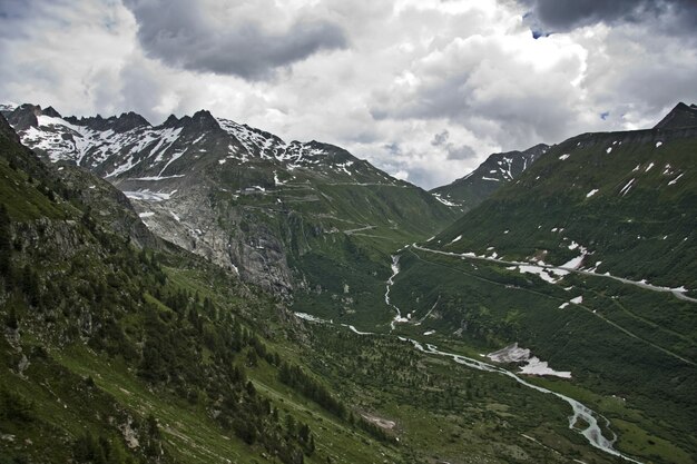 Uitzicht op een bevroren rivier omgeven door groene bergen onder een bewolkte hemel