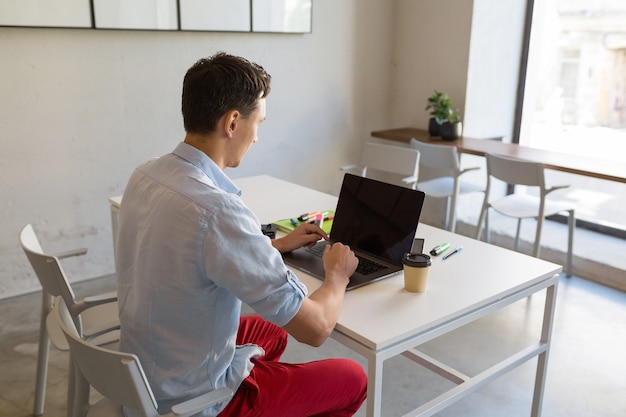 Uitzicht vanaf de achterkant op jonge man aan het werk in co-working kantoorruimte