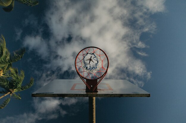 Gratis foto upshot van een basketbalring met een vliegtuig zichtbaar door het mandgat in de hemel