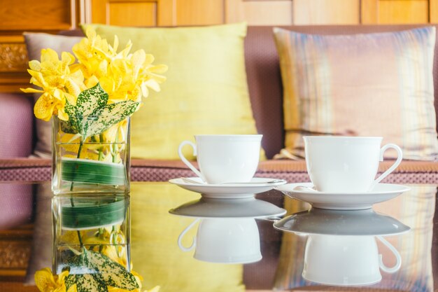 Vaas bloem en witte koffiekop op tafel en kussen op de bank