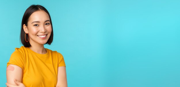 Vaccincampagne van covid19 Jonge mooie gezonde Aziatische vrouw die schouder met pleisterconcept vaccinatie toont die zich over blauwe achtergrond bevindt