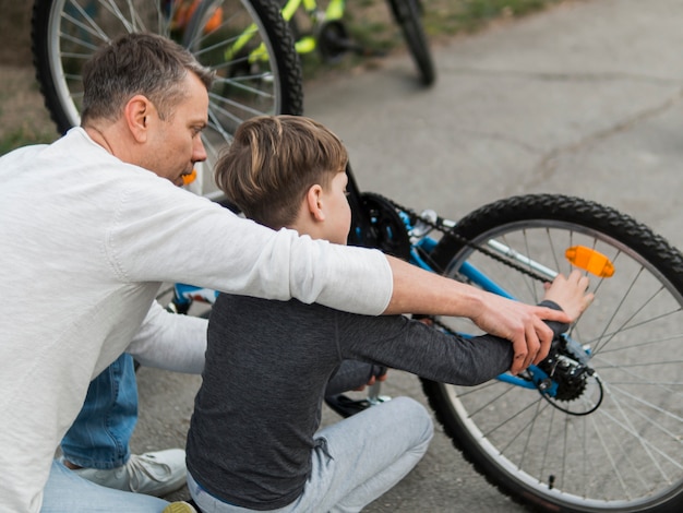 Vader die zijn zoon onderwijst die de fiets over de schoudermening bevestigt