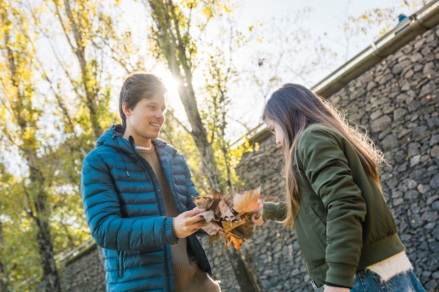 Gratis foto vader en dochter die droge de herfstbladeren voor steenmuur houden