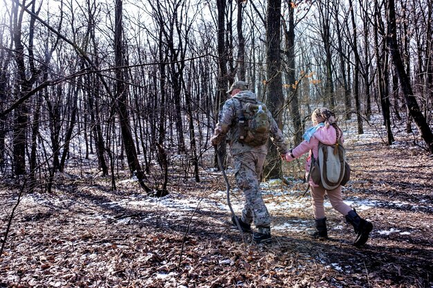 Vader en zijn dochter wandelen in het vroege winterbos, gekleed in camouflage-trekkingkleding