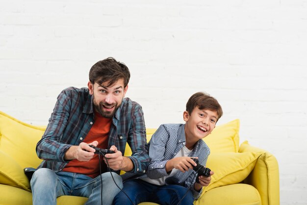 Vader en zoon zittend op een bank en spelen op console
