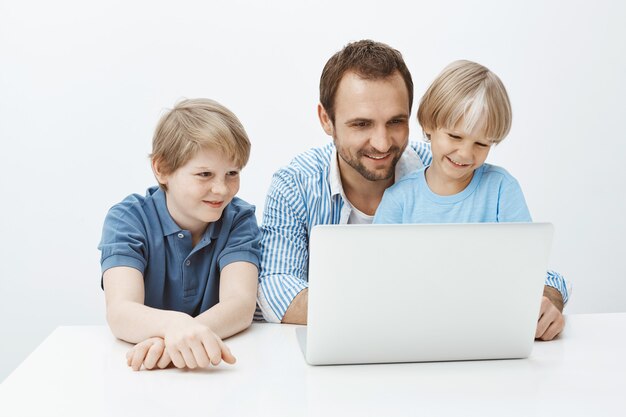 Vader herinnert zich gelukkige herinneringen aan een zomervakantie met zoons. Portret van tevreden zorgeloze familie van jongens en vader zittend aan tafel in de buurt van laptop