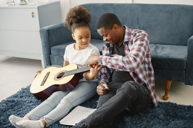 Vader met dochter op bank. Meisje met een gitaar. Gitaar leren.