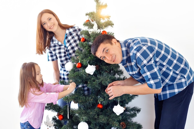Vakantie, ouders en vieren concept - gelukkige familie versieren van een kerstboom met kerstballen in de woonkamer op witte achtergrond.