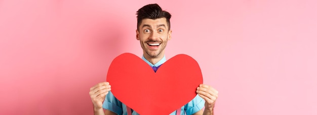 Gratis foto valentijnsdag concept romantische man die verliefd wordt met een groot rood hart en een glimlachende standin