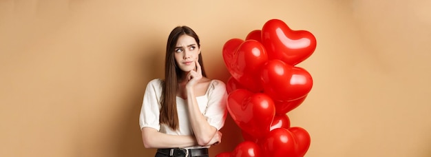 Gratis foto valentijnsdag en liefdesconcept peinzende vrouw in trendy kleding en make-up denkend en fronsend toilet