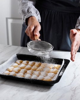 Vanillekipferl-koekje coaten met suikerstof met behulp van zeef, vers zelfgebakken kerstkoekjes op tafel. populair als putri salju in indonesië