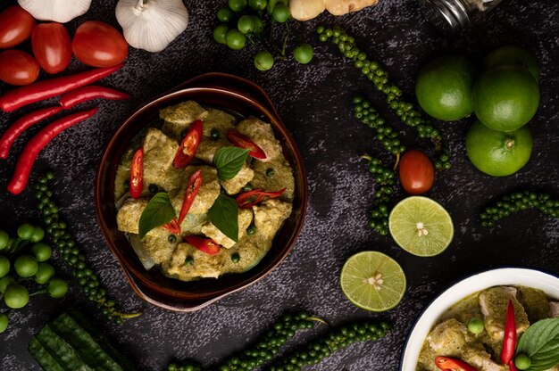 Varkensvlees groene curry in een bruine schaal met specerijen op een zwarte cement achtergrond