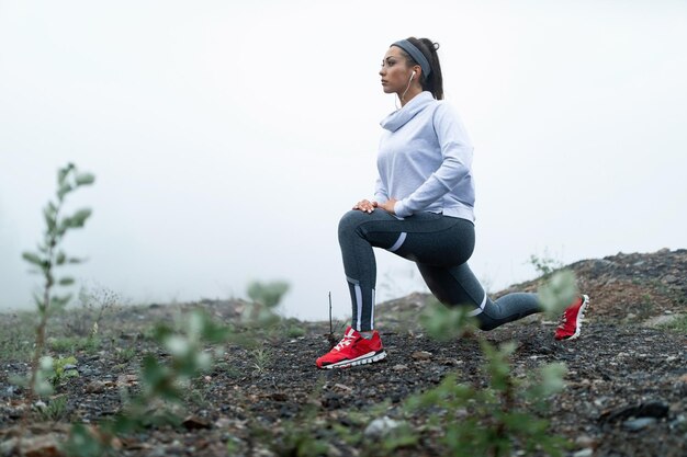 Vastberaden sportvrouw die zich uitstrekt in uitvalpositie op een klif tijdens mistige ochtend