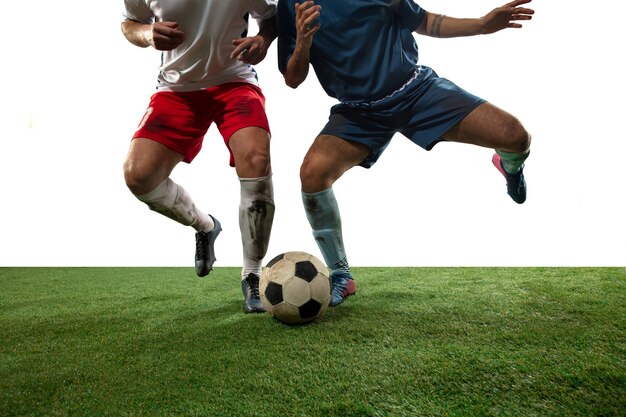 Vechten. Close-up benen van professionele voetbal, voetballers vechten voor bal op veld geïsoleerd op een witte muur. Concept van actie, beweging, hoog gespannen emotie tijdens spel. Bijgesneden afbeelding.