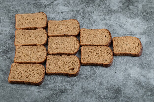 Veel sneetjes bruin brood op een grijze ondergrond.