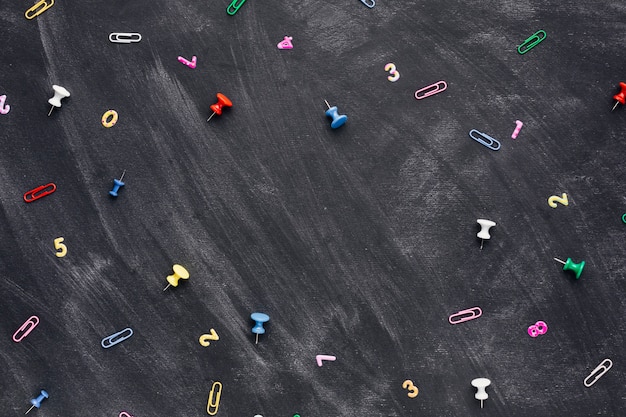 Veelkleurige cijfers en paperclips met pushpins verspreid op schoolbord