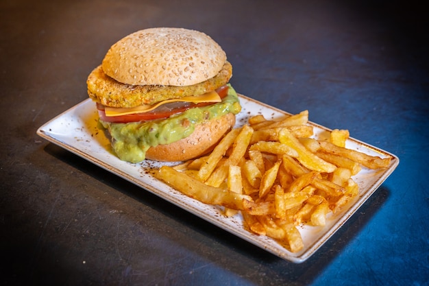 Vegan burger met guacamole en friet op een witte plaat op een zwarte achtergrond