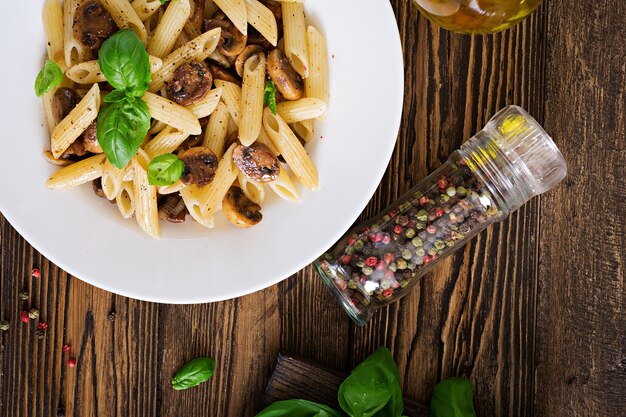 Vegetarische Plantaardige pasta penne met champignons in witte kom op houten tafel. Veganistisch eten. Bovenaanzicht