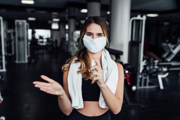 Veilige sport, mooi meisje in de sportschool met een beschermend masker op haar gezicht en met een ontsmettingsmiddel