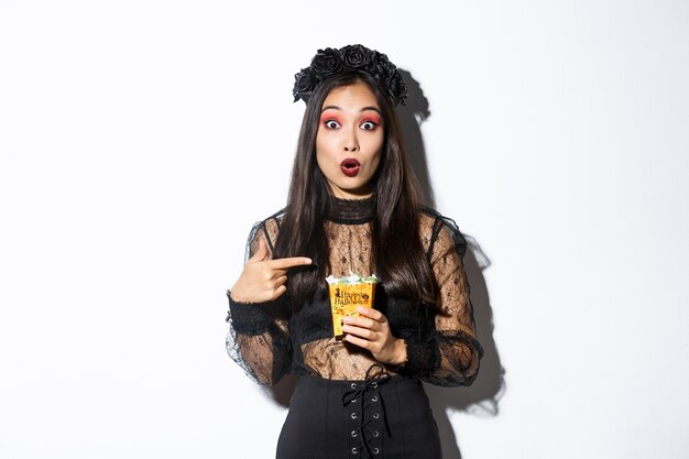Verbaasd Aziatisch meisje dat camera bekijkt terwijl vinger naar snoepjes wijst