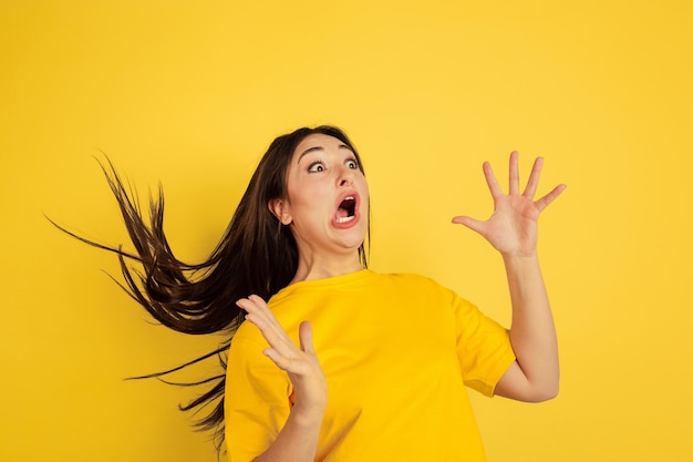 Verbaasd, gek. Portret van de blanke vrouw geïsoleerd op gele studio achtergrond. Mooie vrouwelijke brunette model in casual stijl. Concept van menselijke emoties, gezichtsuitdrukking, verkoop, advertentie, copyspace.