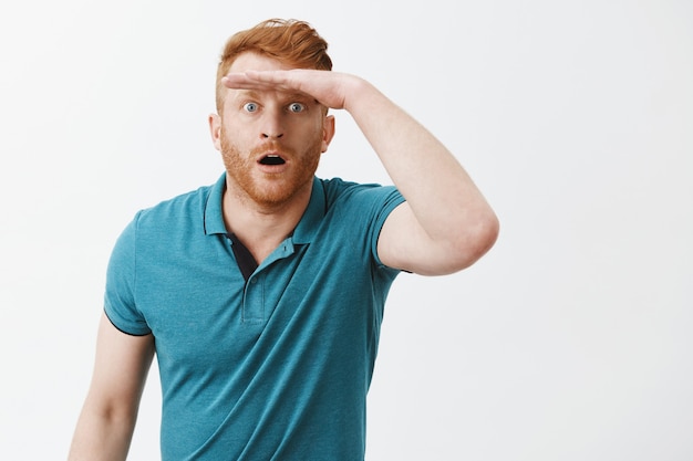 Gratis foto verbaasde en verbaasde blanke man in groene polo met palm op voorhoofd en hijgend met geopende mond terwijl hij op afstand staart en ver weg iets indrukwekkends ziet